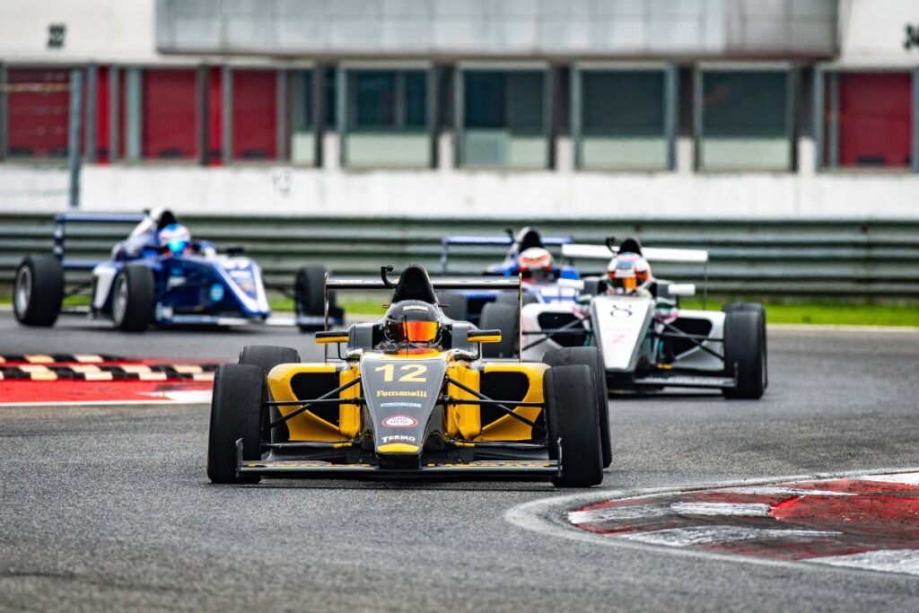 Yellow formula racing car labelled number 12 with two other cars in the background